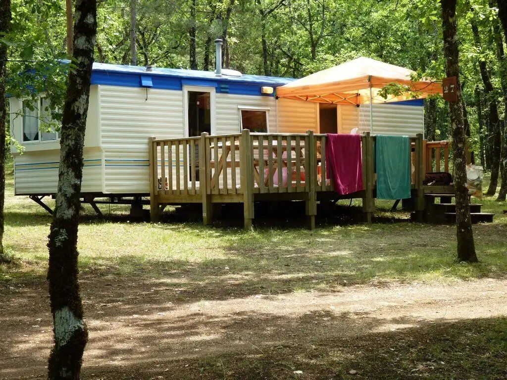 A mobile home with a deck and a covered area, surrounded by trees.