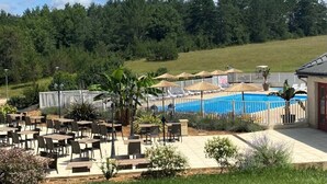A poolside area with outdoor seating, a pool, and a view of a forested hill. - ZEcamping 3* pataugeoire piscine locatif TV 31m2 5 pers (Pezuls)