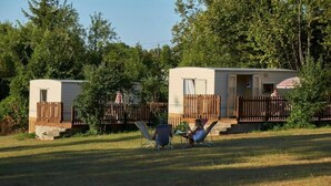 Two mobile homes with wooden fences, a lawn, and trees in the background. - ZEcamping 3* pataugeoire piscine locatif TV 31m2 5 pers (Pezuls)