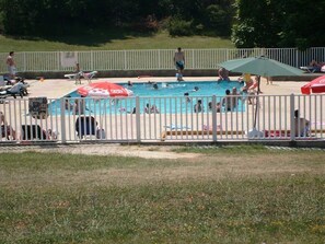 Een zwembad met mensen die zwemmen en zonnebaden. Er staan parasols en ligbedden.