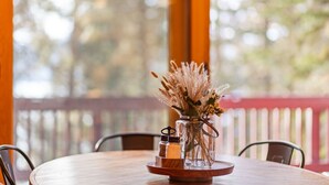 Une table ronde en bois sur laquelle se trouve un vase en verre contenant des plumes de jarre séchées et de petites fleurs, une bougie et un petit pot.