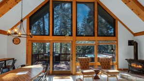 Une pièce spacieuse avec un grand plafond en bois, une cheminée et une vue sur une forêt, visible à travers de grandes fenêtres.