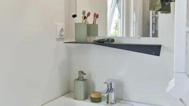 Une salle de bain moderne avec un lavabo blanc, un miroir au-dessus et une étagère contenant des articles de toilette.