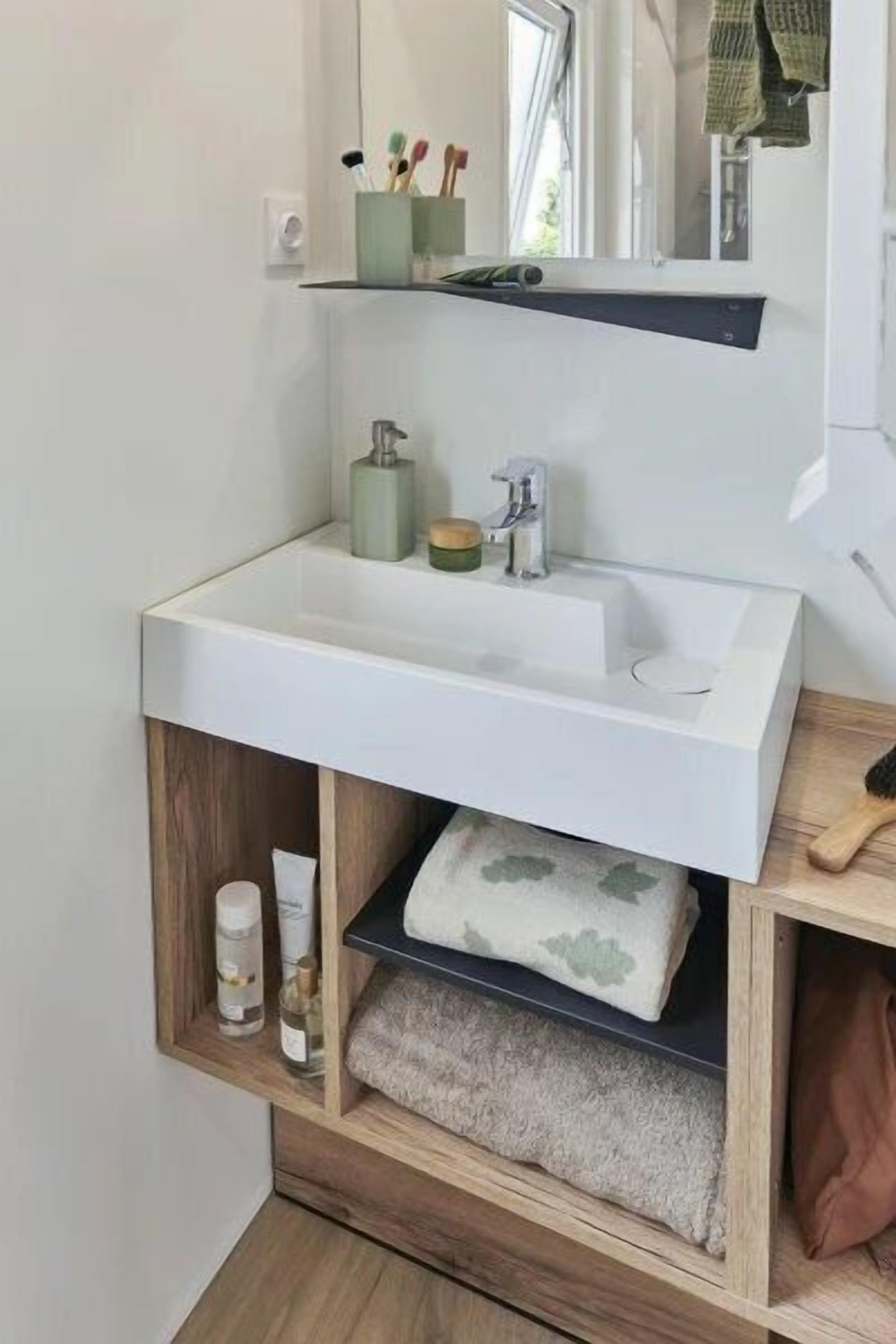 Un baño moderno con un lavamanos blanco, un espejo encima y un estante con artículos de aseo.