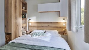 Ein Schlafzimmer mit einem hölzernen Kopfteil, einem Bett mit weißer Bettwäsche, einem Nachttisch mit Lampe und einer eingebauten Holzregaleinheit.