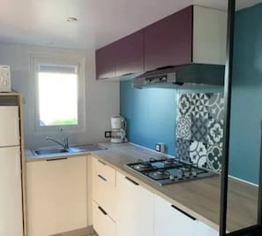 A modern kitchen with a gas stove, a coffee maker, and a window. - ZEcamping 4 étoiles animaux acceptés piscine bar et restaurant (Saint-Georges-d'Oléron)