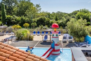 A swimming pool area with a water slide, lounge chairs, and a thatched-roof structure.
