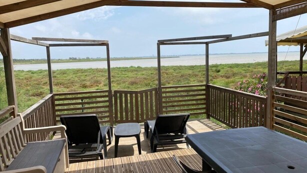 Eine Terrasse im Freien mit Blick auf ein Gewässer, Holzmöbel und einem überdachten Bereich.