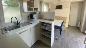 Eine kleine Küche mit Spüle, Schränken und einer Mikrowelle. Es gibt eine Essecke mit Tisch und Stühlen.