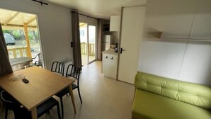 A room with a wooden dining table, chairs, a green sofa, a white cabinet, and a sliding door leading to a balcony.
