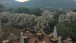 Une terrasse extérieure avec des tables et des chaises rondes, entourée de fleurs blanches en pleine floraison, offrant une vue sur un paysage montagneux.