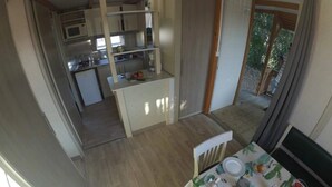 A compact kitchen with a microwave, stove, and refrigerator. A dining table with a cactus-themed tablecloth is set up in the dining area. - ZEcamping 3* piscine 1km plage locatif 25m2 5 pers (Viggianello)
