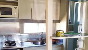 A compact kitchenette with a microwave, stove, sink, and a small refrigerator. - ZEcamping 3* piscine 1km plage locatif 25m2 5 pers (Viggianello)