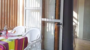 Een overdekt terrasgedeelte met een tafel gedekt voor twee personen, witte plastic stoelen en een glazen schuifdeur naar een buitenruimte.