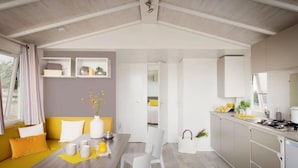 Una cocina moderna con armarios blancos, una zona de comedor con mesa amarilla y una sala de estar con sofá amarillo.