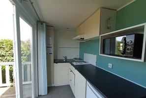 Een kleine keuken met een zwart aanrecht, witte kasten en een raam met zonwering.