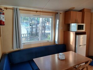 A compact kitchenette with a microwave, refrigerator, and a window with curtains.