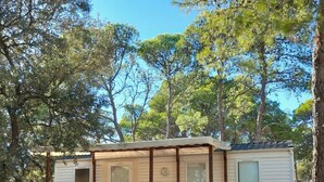 A mobile home with a wooden deck and a small porch, surrounded by trees. - ZEcamping 3 étoiles familial toboggans dog friendly locatif BBQ clim (Fabrezan)