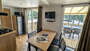 A compact kitchen with a refrigerator, microwave, and stove, a dining area with a table and chairs, and a balcony with outdoor seating. - ZEcamping 3* animé toboggans animaux acceptés locatif TV LV BBQ 31m2 (Fabrezan)