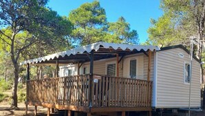 Una casa móvil con una terraza de madera y un porche cubierto, rodeada de árboles.