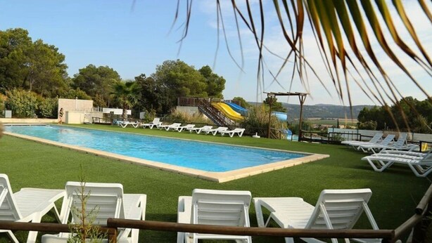 A swimming pool with a slide, surrounded by white lounge chairs and greenery.