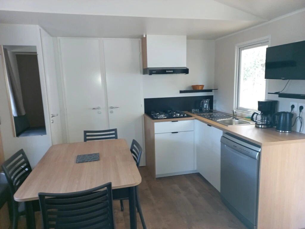 A compact kitchen with white cabinets, a wooden dining table, and a built-in dishwasher.