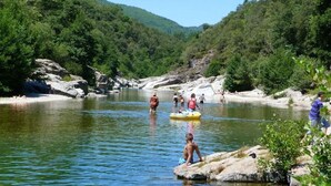A river with people engaging in water activities, surrounded by lush greenery and rocky terrain.