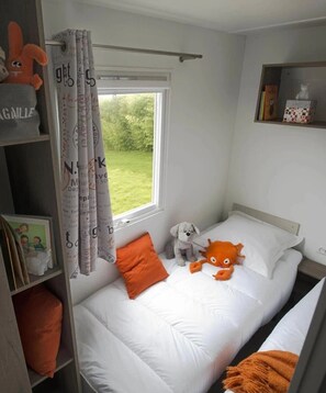 Ein Schlafzimmer mit Bett, einem Fenster mit Vorhängen, einem Regal mit Büchern und einem Stofftier.