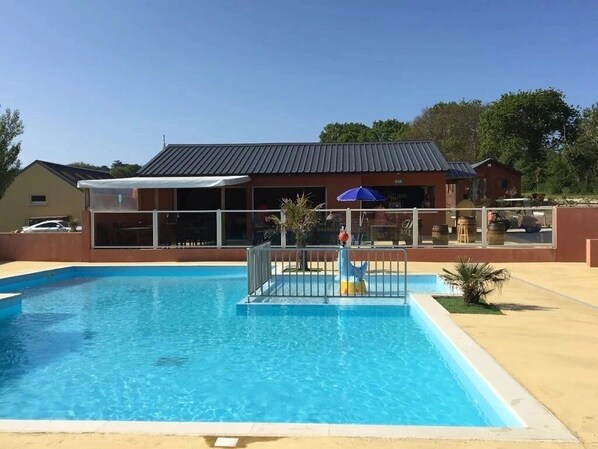 Ein Schwimmbad mit umzäunter Deckbereich, einem überdachten Sitzbereich und einem Gebäude mit Metallbedachung im Hintergrund.