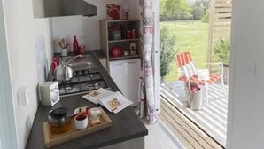 A small kitchenette with a gas stove, a sink, and a window overlooking a garden. - ZEcamping 3* piscine couverte animaux acceptés animations locatif TV (Erquy)
