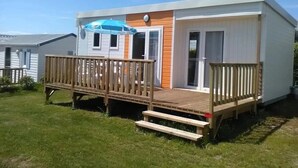 A single-story mobile home with a wooden deck, a covered outdoor seating area, and a sliding glass door. - ZEcamping 3* piscine couverte animaux acceptés animations locatif TV (Erquy)