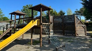 Une aire de jeux avec un toboggan jaune, un filet d’escalade et des structures en bois.