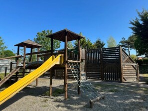 A playground with a yellow slide, climbing structures, and a wooden playhouse.