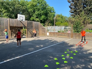An outdoor basketball court with a wooden fence, a basketball hoop, and green triangular markers on the ground.