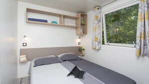 Quarto com cama, mesas de cabeceira, janela com cortinas e prateleiras embutidas.
