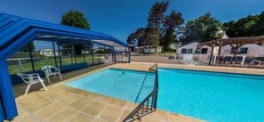 A swimming pool with a blue canopy and white chairs.