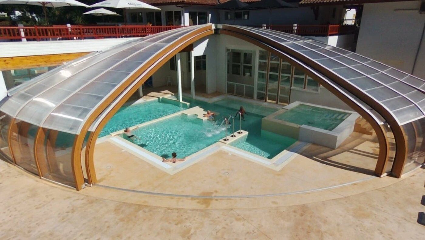 A covered swimming pool with a glass roof, multiple smaller pools, and a sandy floor.