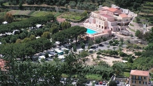 Oversigtsbillede af et resort med en central bygning, en swimmingpool og grøn bevoksning omkring.