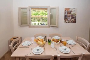 Un coin repas avec une table mise pour le petit-déjeuner, comprenant du pain, des viennoiseries et un panier de fruits.