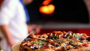 Une pizza garnie de divers ingrédients, une personne floue à l’arrière-plan et un four flou.