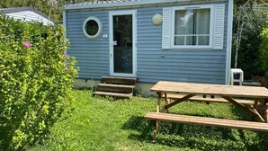 A small blue cabin with a front door, a round window, and a picnic table in the foreground.