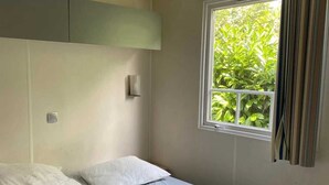 A bedroom with a bed, a window with curtains, and a wall-mounted light fixture.