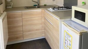 A compact kitchen with wooden cabinets, a sink, a stove, and a microwave.