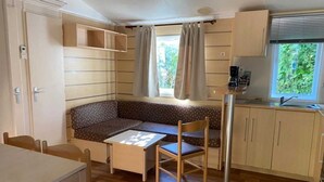 Et kompakt og velbelyst værelse med trægulv, sofa, spisebord og et tekøkken.