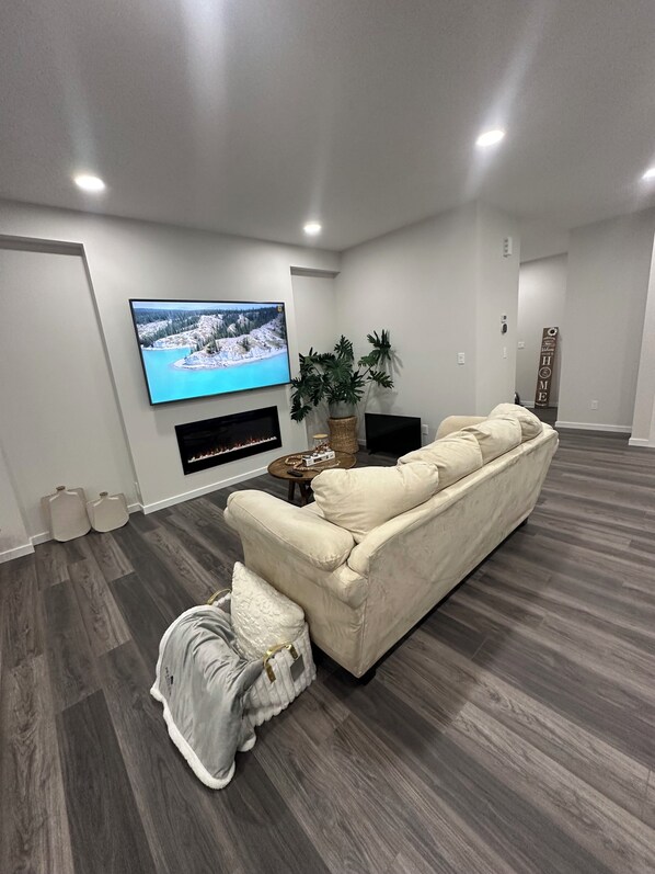 Una sala de estar moderna con un televisor de pantalla plana grande montado en la pared, un sofá color beige, una mesita de centro y una planta en maceta.