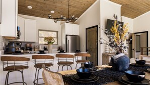 A modern kitchen with white cabinets, a stainless steel refrigerator, and a dining area with a wooden table and bar stools.