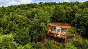 A wooden cabin with a balcony, surrounded by dense forest.