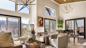A spacious living room with large windows, a chandelier, and a dining area with a view.