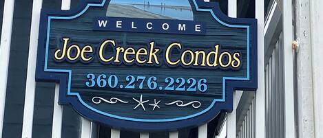 A welcome sign for Joe Creek Condos with a contact number.