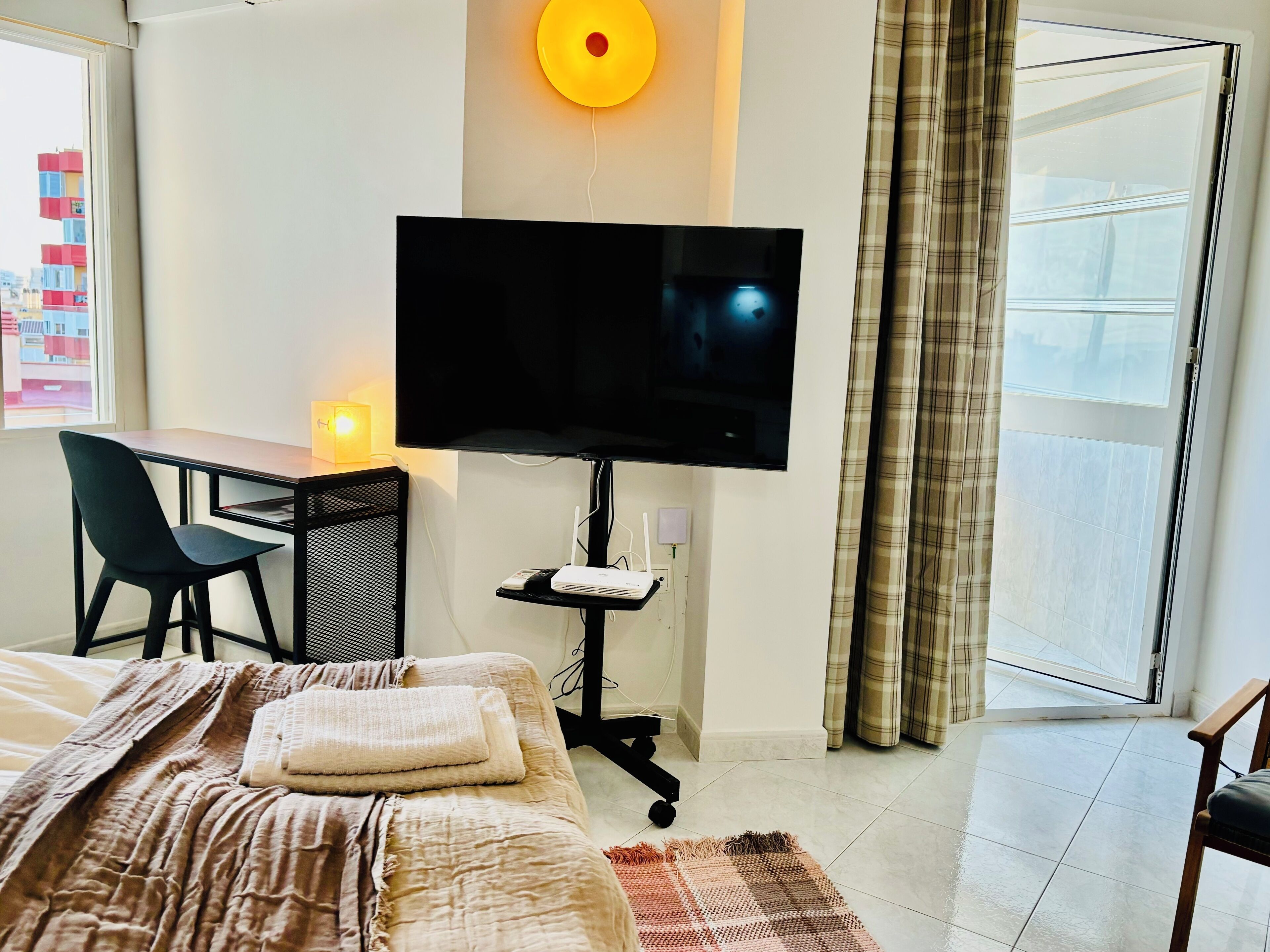 A hotel room with a bed, a desk with a chair, a television, and a window with curtains.